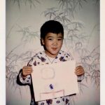 Corey Okada, age five, with drawing of NASA's Launch Control Center, Cape Kennedy, FL, complete with Saturn V rocket on the monitor (December 1969).