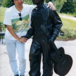 Corey Okada with bronze statue Elvis at 13 at Elvis Presley Birthplace Park, Tupelo, MS (2025).